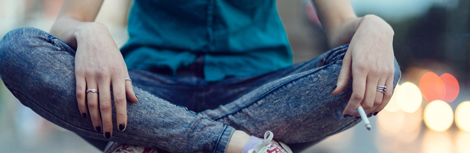 Person sits cross-legged holding cigarette