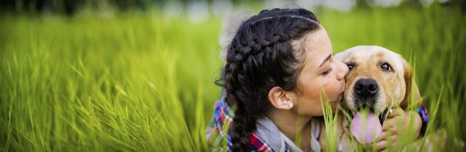 Woman in field of grass gives dog a kiss