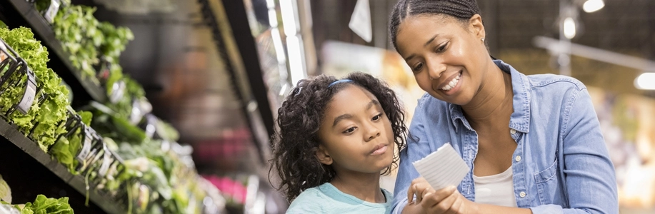 Black mom and daughter look at grocery list in vegetable aisle